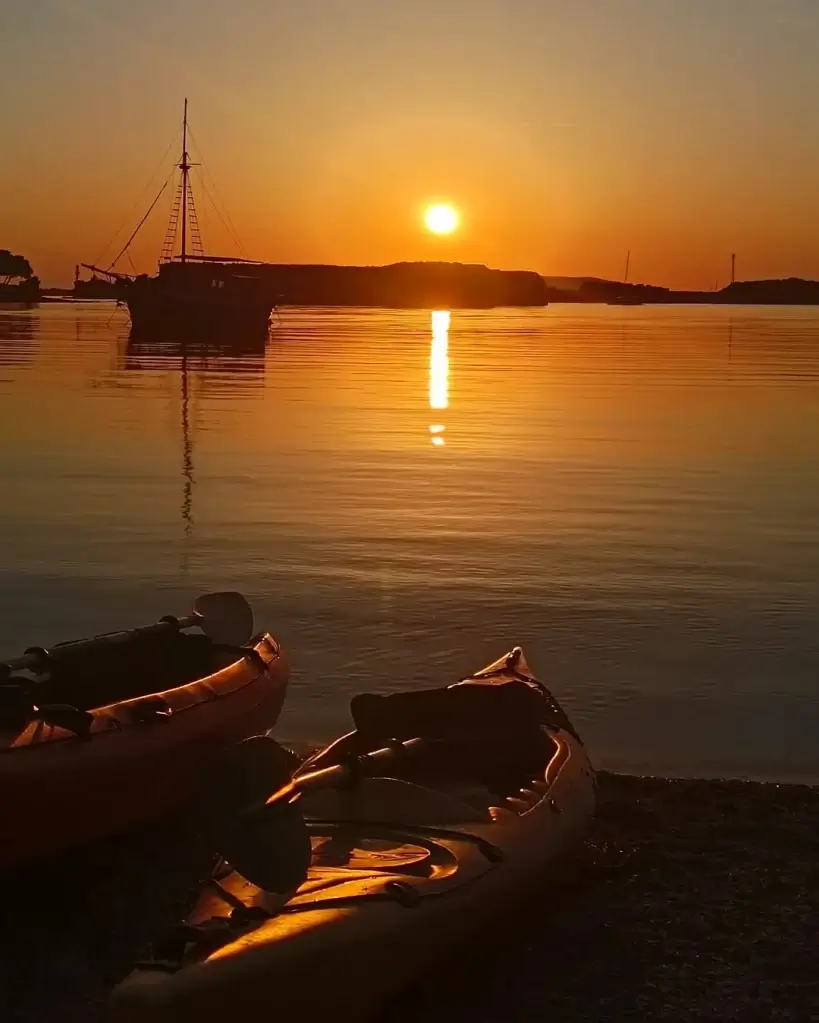 Sunset kayaking scene with kayaks on calm Adriatic waters near Šibenik.