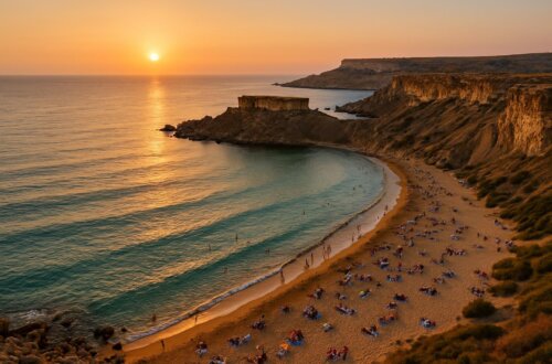 Aerial view of Golden Bay Malta at sunset showing golden sand beach, turquoise Mediterranean waters, limestone cliffs, and tourists enjoying Malta's most famous beach