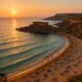 Aerial view of Golden Bay Malta at sunset showing golden sand beach, turquoise Mediterranean waters, limestone cliffs, and tourists enjoying Malta's most famous beach